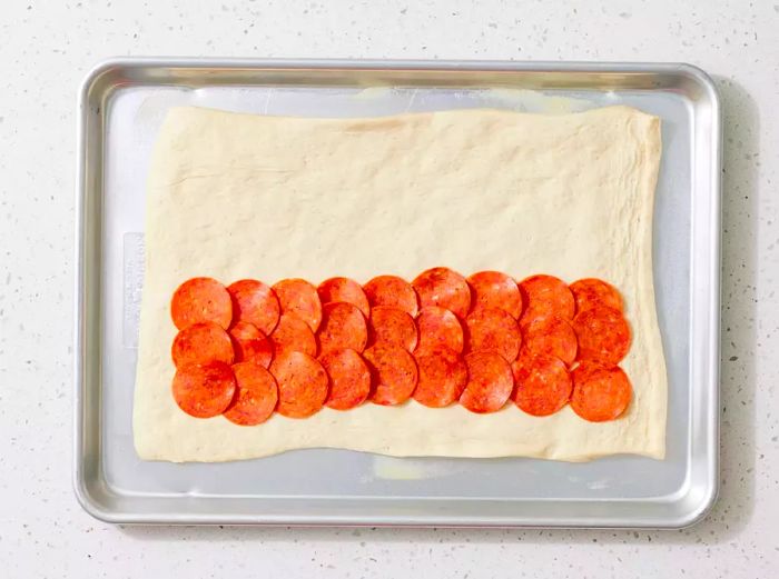 A baking sheet with a flattened piece of pizza dough, topped with pepperoni on the bottom half