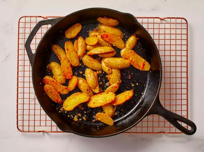 Roasted fingerling potatoes cooling in a skillet on a wire rack.