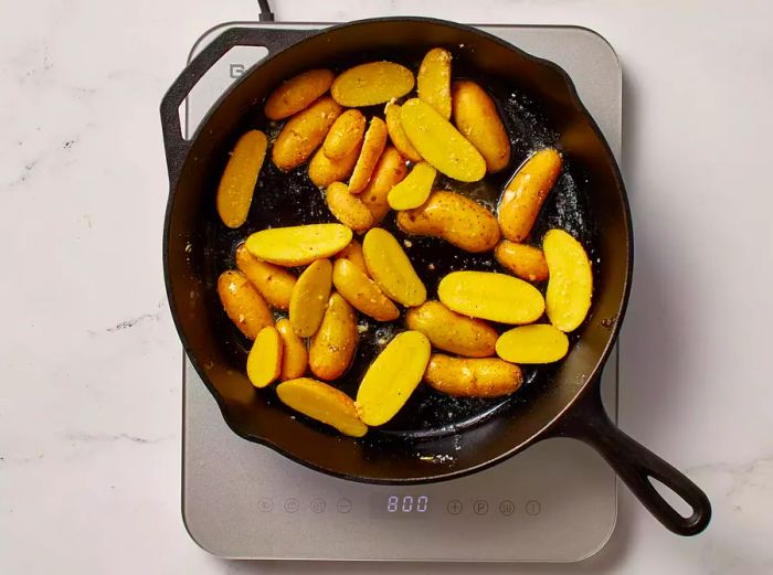 Fingerling potatoes cooking in a skillet on an electric stovetop.