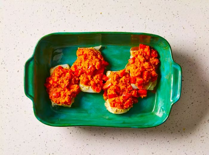 Fish fillets topped with a tomato and herb sauce in a green baking dish