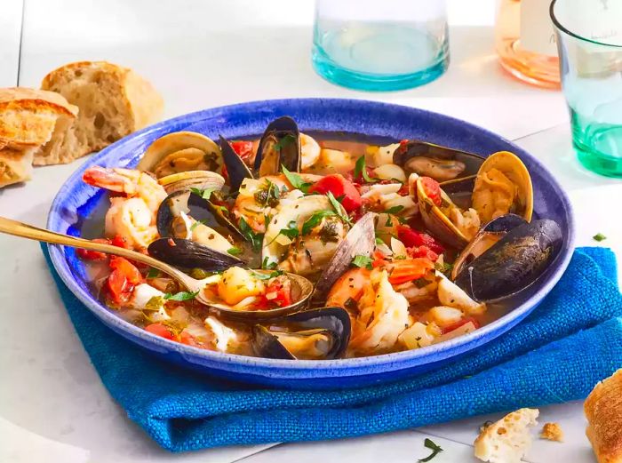 A close-up shot of a bowl of cioppino filled with mussels, clams, and shrimp, all served in a vibrant blue bowl.