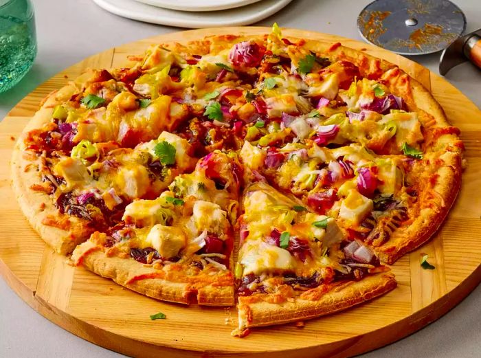 A barbecue chicken pizza placed on a round cutting board, with two slices already cut.