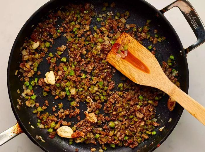 A large skillet with sautéed onions and celery mixed with spices