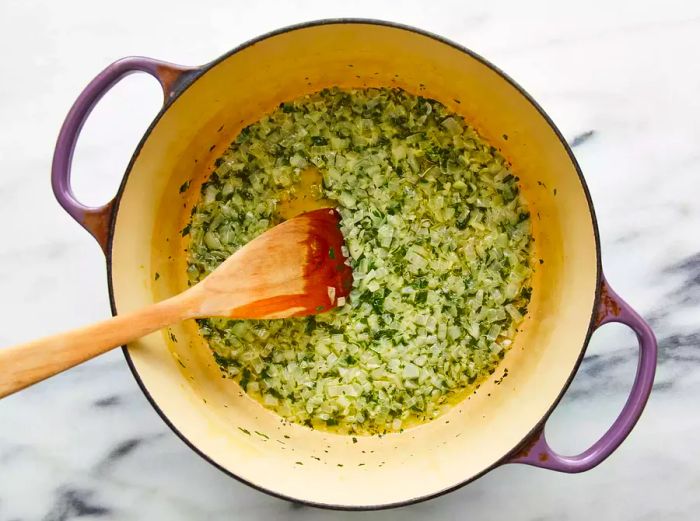 Sauté onions and parsley in a pot, stirring with a spoon.