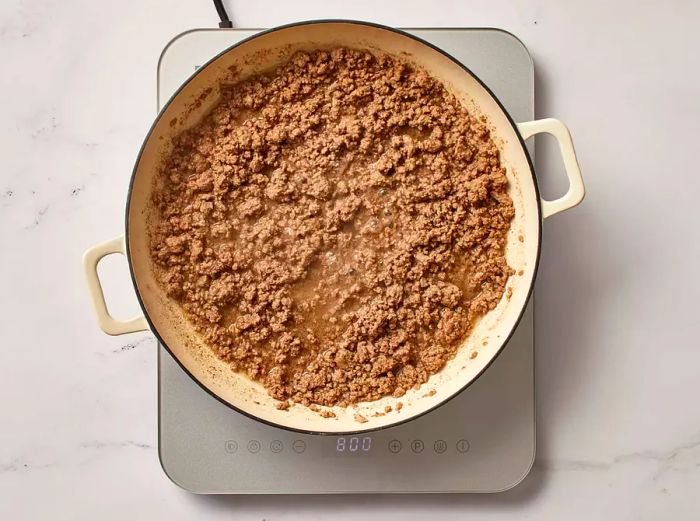 Ground beef cooking in a skillet on an electric stovetop.