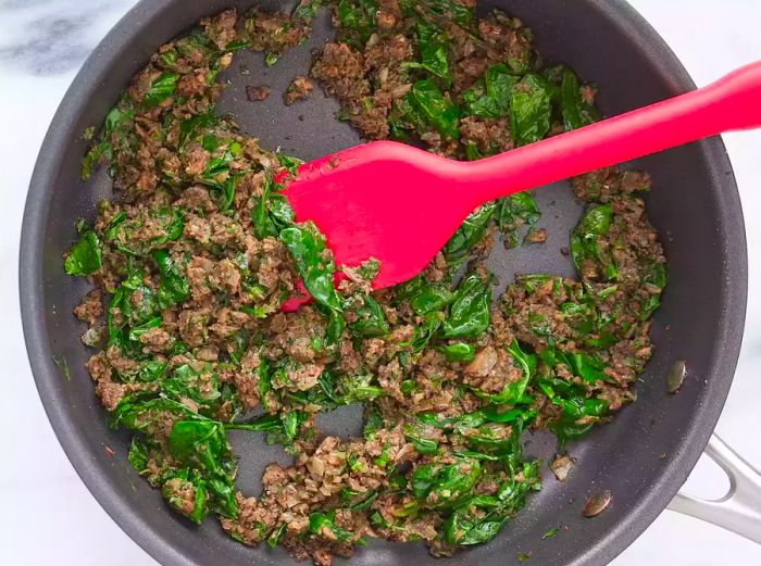 Parsley and spinach are added to the skillet and cooked until the spinach wilts.