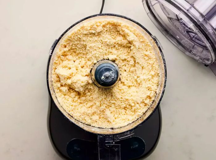 A food processor containing the crumbled pie dough mixture