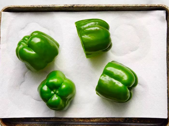 A baking sheet lined with paper towels holding four green bell peppers that have been hollowed out.