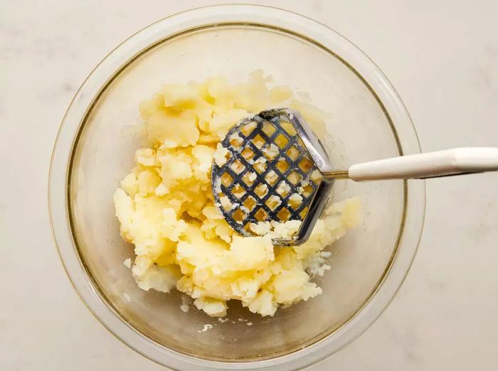 A bowl of smooth mashed potatoes with a potato masher