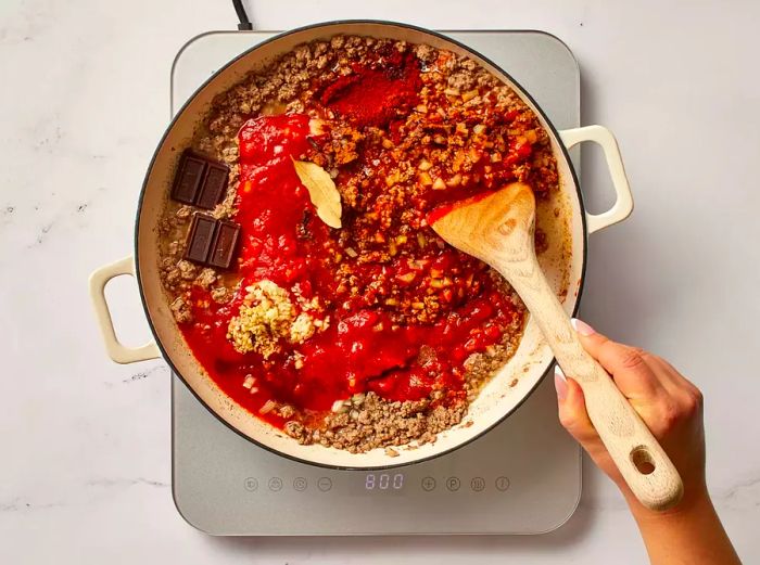 Ingredients being added to the cooked ground beef in a skillet.