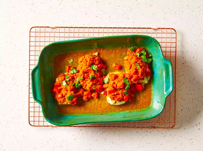 Baked fish fillets with tomato and herb sauce in a green baking dish