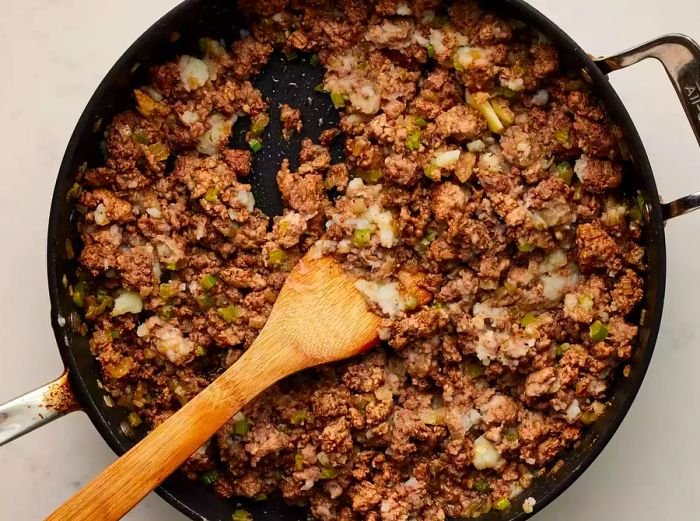 A large pot containing cooked ground beef, ground pork, mashed potatoes, onions, celery, and spices