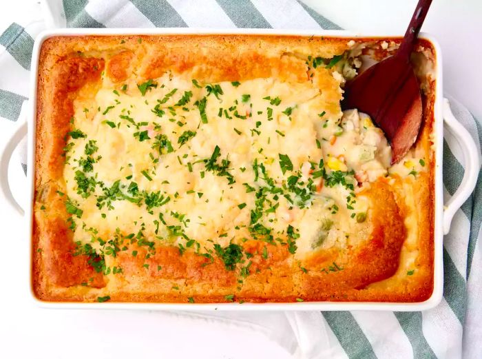 A serving of chicken cobbler in a casserole dish with a spoon resting on the side