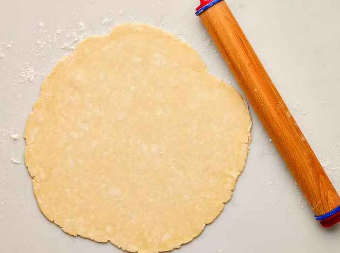 A rolled-out piece of pie dough on a floured surface with a rolling pin beside it