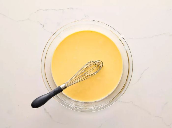 A bowl containing eggs and milk being whisked together.