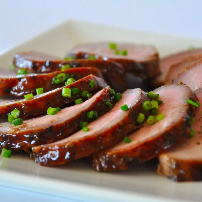 Close-up shot of sliced Asian Pork Tenderloin garnished with green onions on a plate.