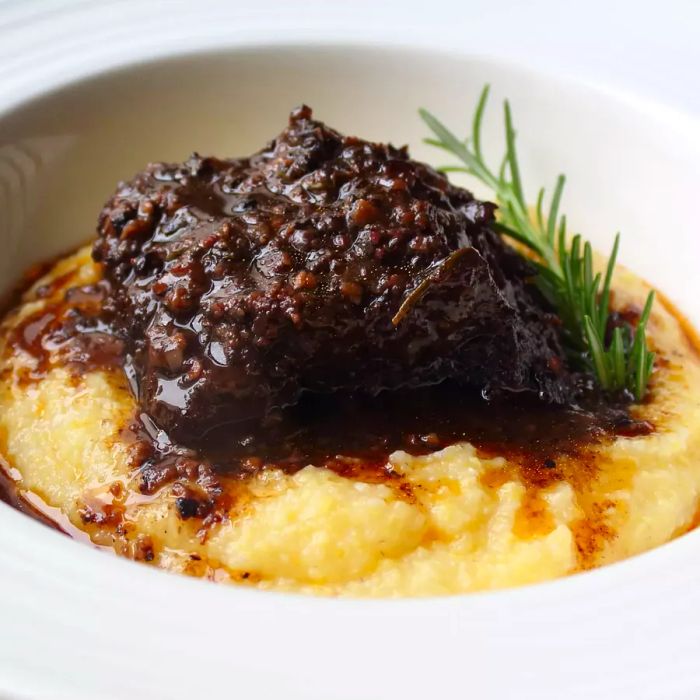 A close-up view of Peposa Dell'Impruneta served over polenta, garnished with fresh herbs, in a white bowl.