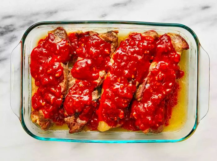 Ribs smothered in barbecue sauce in a clear glass baking dish