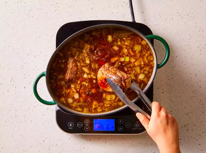 A hand using tongs to carefully place beef short ribs into a pot on the stovetop.