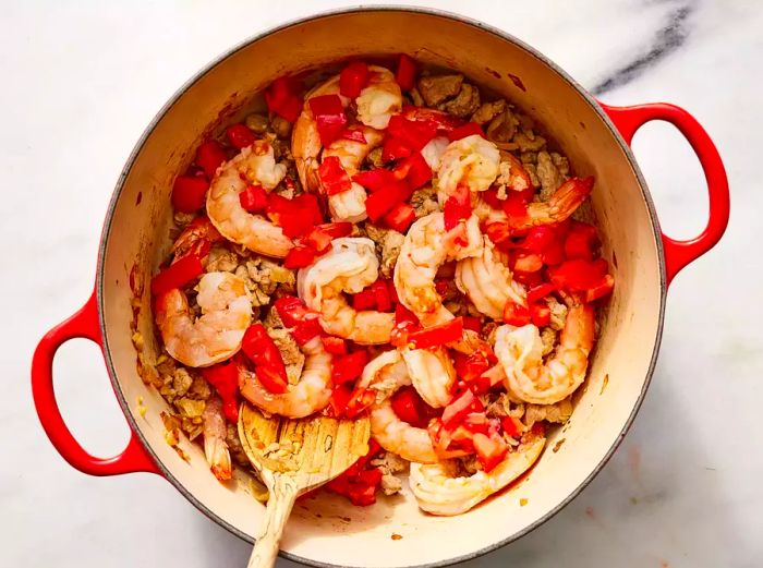 Bird's eye view of onions, garlic, pork, shrimp, and tomatoes cooking in a skillet.