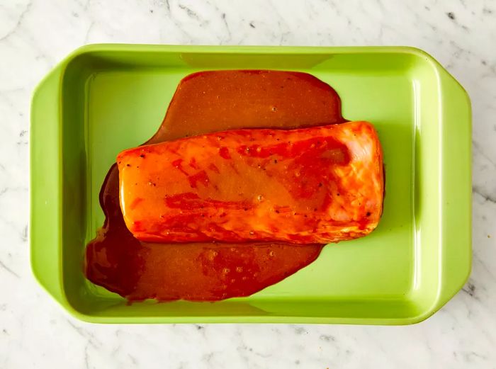 Pork tenderloin placed in a baking dish, with marinade poured on top.