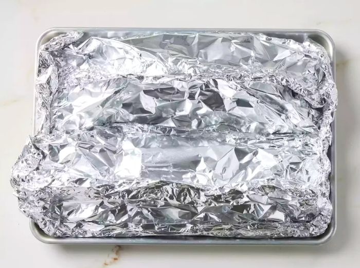 Two tightly sealed foil packets placed on a baking sheet, ready to cook.