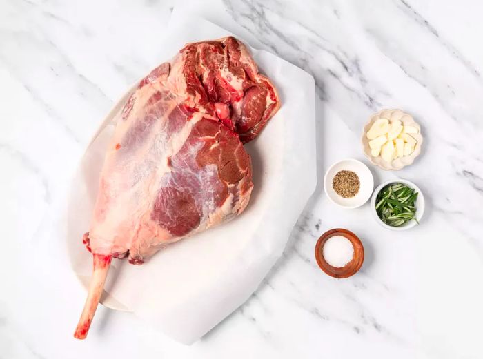 Raw leg of lamb seasoned with garlic and spices, placed on parchment paper.