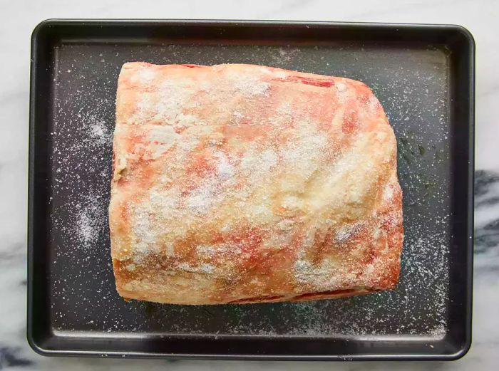 A roast coated in kosher salt, resting on a baking dish.