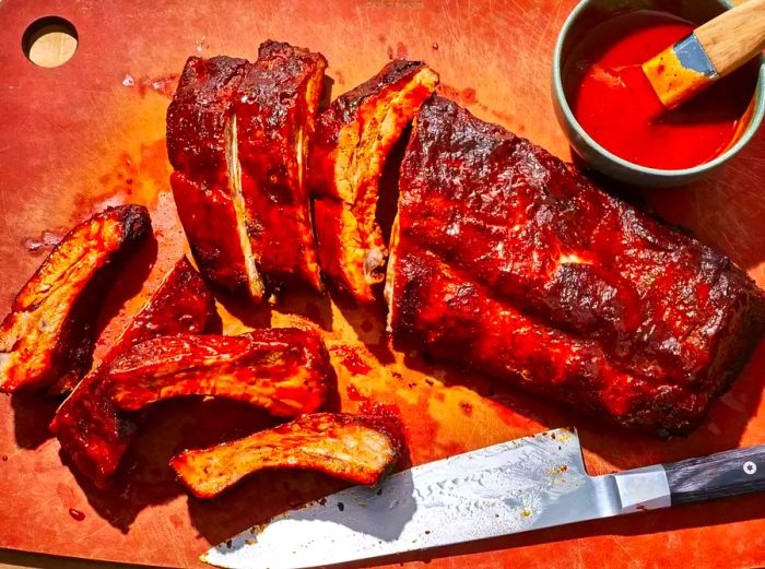 Oven-baked baby back ribs with a knife and a bowl of barbecue sauce