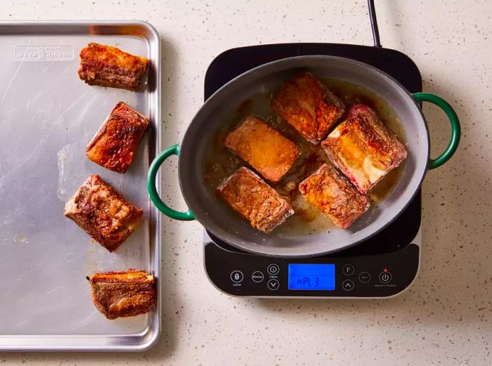 Beef short ribs arranged on a baking sheet and in a pot on the stovetop.