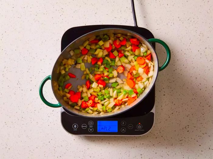 Onions, carrots, and celery cooking together in a pot on the stove.