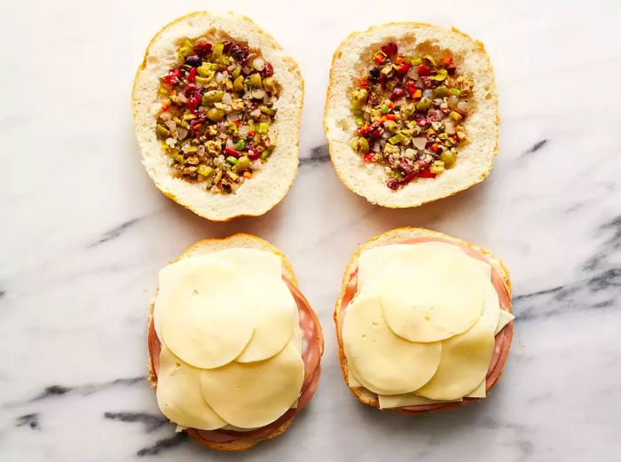 A top-down view of four slices of bread, with the top two covered in olive salad and the bottom two layered with salami and cheese.