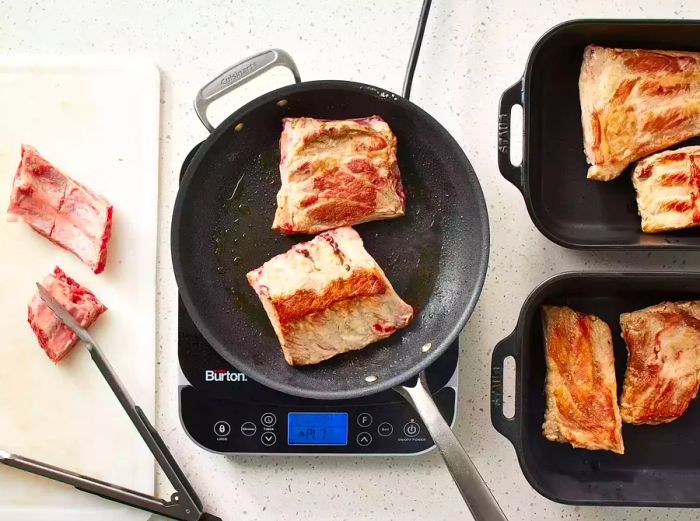 Ribs cooking in a skillet beside ribs on a cutting board and in roasting pans