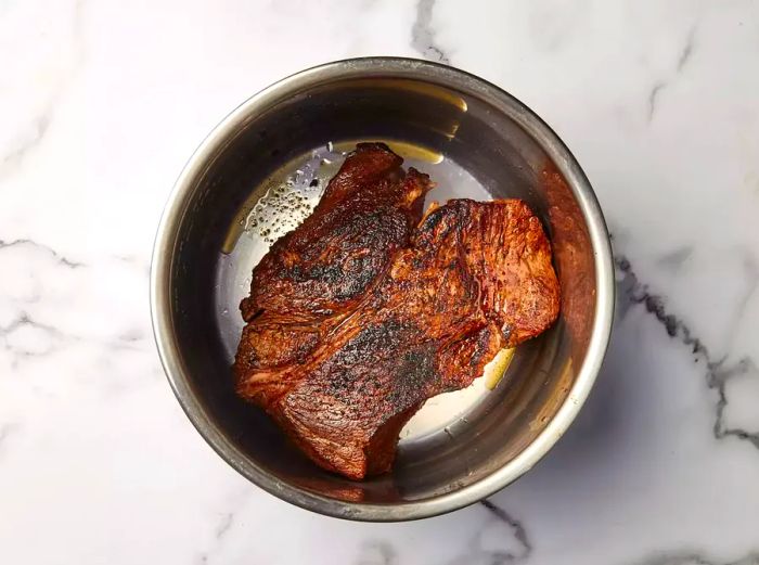 A browned boneless beef chuck roast in a pressure cooker