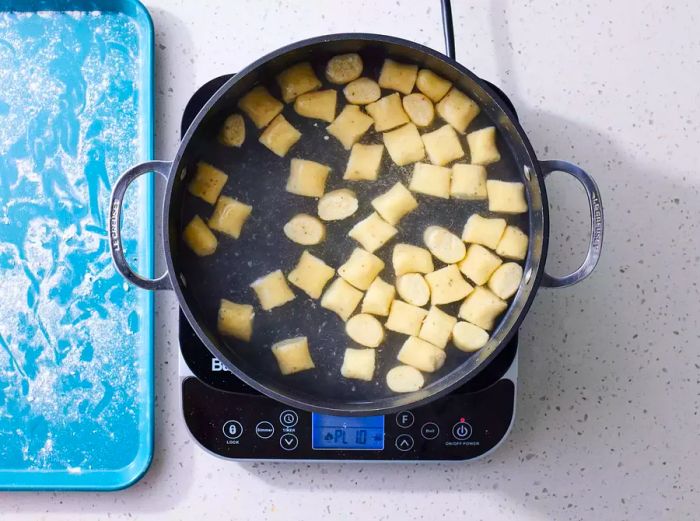 Ricotta Gnocchi cooking in a pot of water on the stove, next to a baking sheet