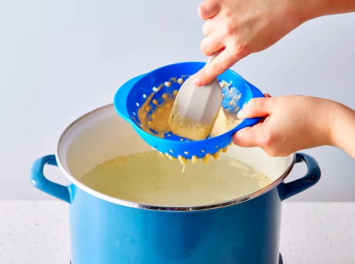 Batter being pressed through the spaetzle press and dropped into the boiling water.