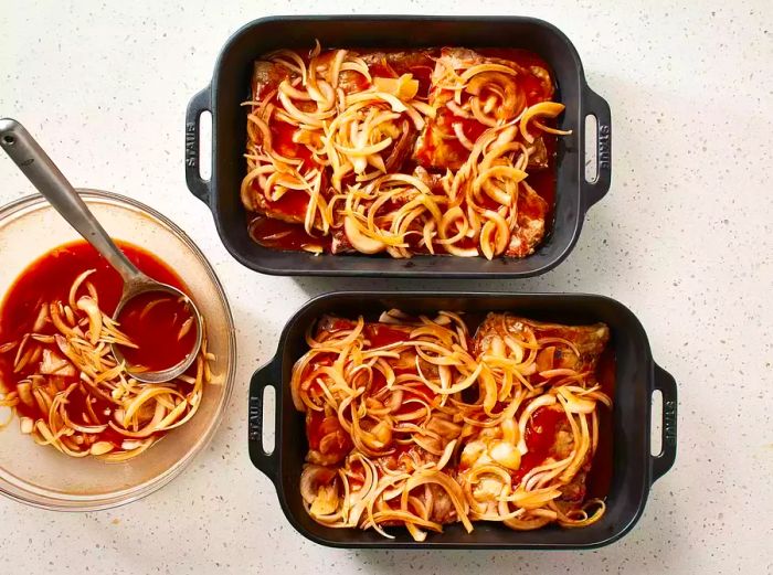 Oven-Baked BBQ Ribs in roasting pans next to a bowl of sauce and a ladle