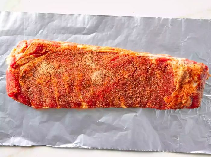 A rack of pork ribs seasoned and placed on a sheet of aluminum foil