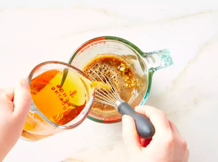 Beer being poured and whisked together with garlic, honey, Worcestershire sauce, and mustard in a mixing bowl.