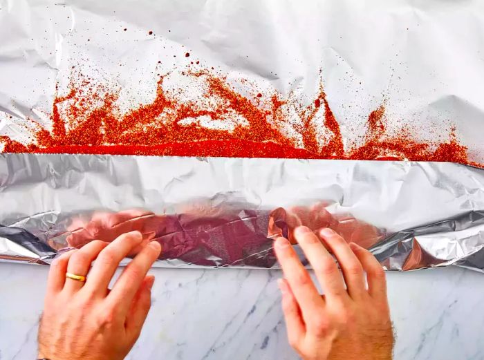 Hands wrapping the seasoned rack of ribs in aluminum foil