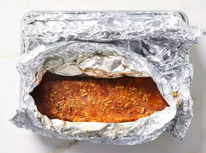 An open foil packet revealing a perfectly baked rack of pork ribs.