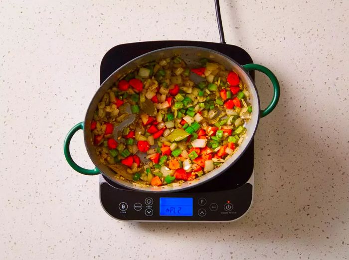 Vegetables with garlic, thyme, and bay leaves cooking in a pot on the stove.