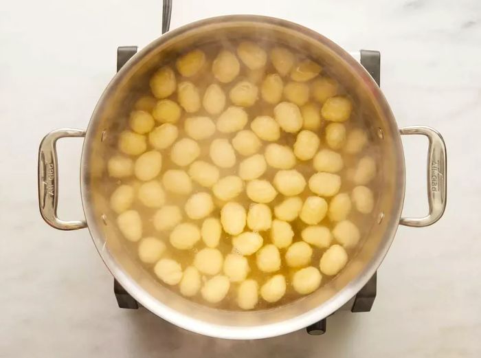 Gnocchi cooking in water, rising to the surface when done.