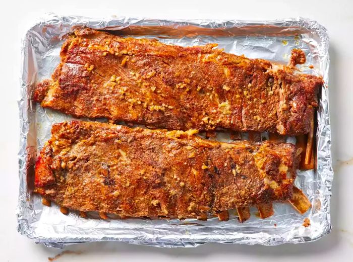 Two racks of pork spareribs resting on a foil-lined baking sheet, ready for the next step.