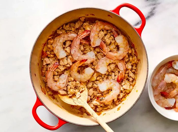 Bird's eye view of onions, garlic, pork, and shrimp cooking together in a skillet.