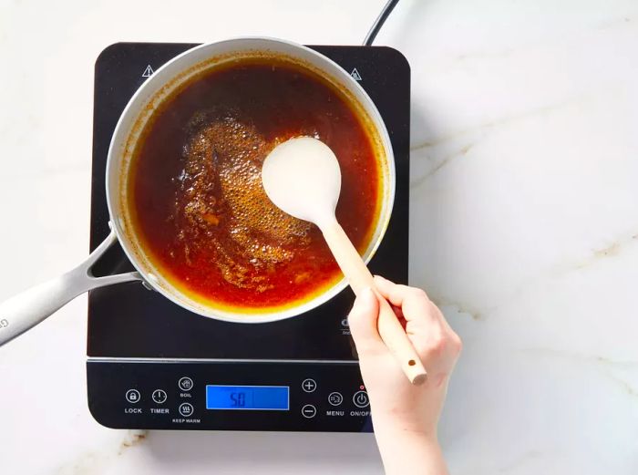 A pot of rib sauce being stirred with a spoon as it thickens.