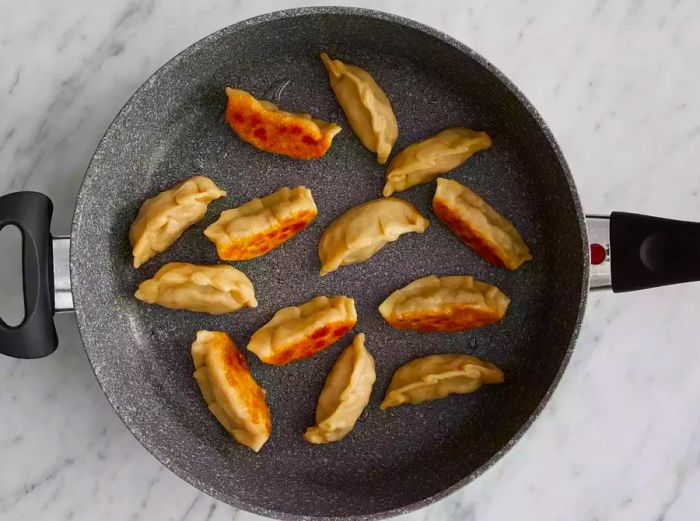 An overhead shot of pot stickers cooking in a pan.