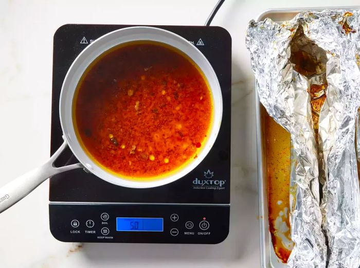 A pot of reserved sauce placed next to a baking sheet with an open foil packet.