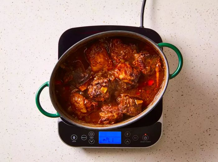 Braised beef short ribs simmering in a pot on the stove.