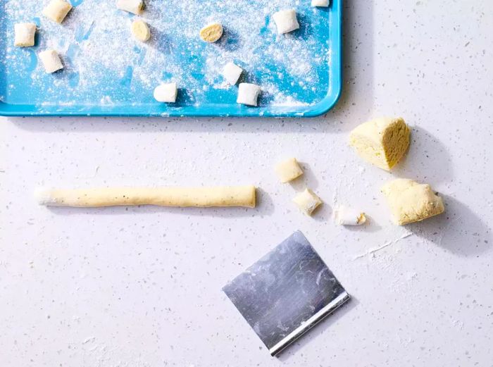 Ricotta Gnocchi dough cut into pieces on a countertop, with flour scattered on a baking sheet